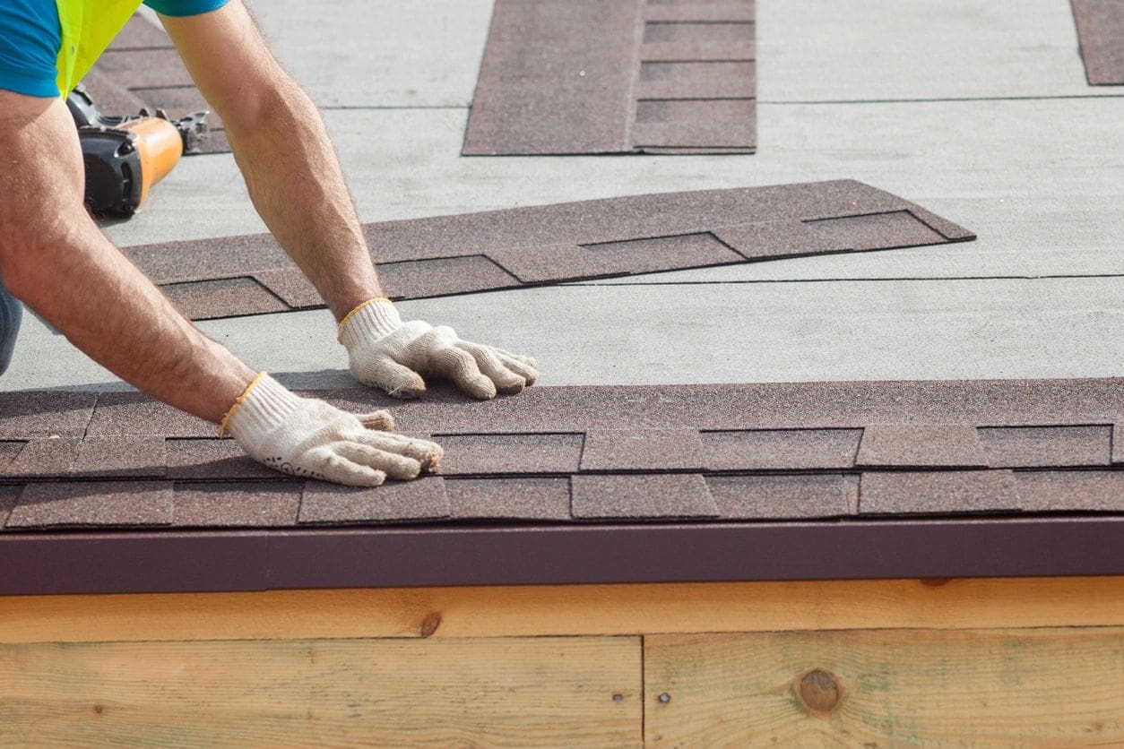 A person with gloves on working on the roof of a house.